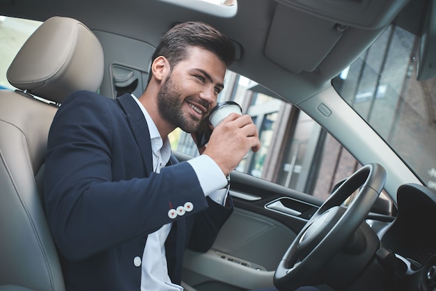 Joven empresario atractivo en coche beber café y hablar sobre