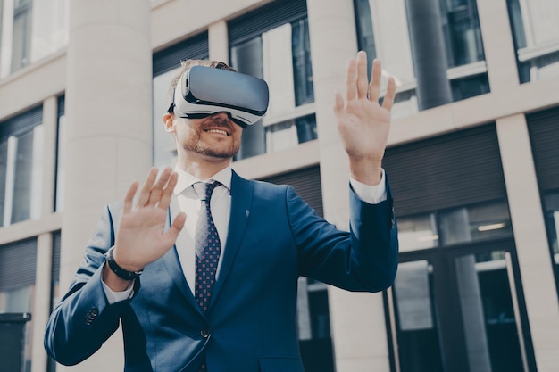 Joven empresario con barba vestido con traje formal azul probando gafas vr al aire libre