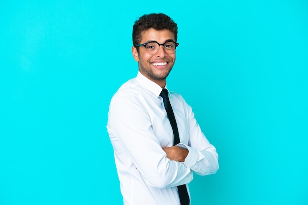 Joven empresario brasileño aislado de fondo azul con los brazos cruzados y mirando hacia adelante