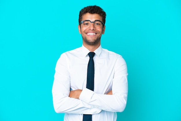 Joven empresario brasileño aislado de fondo azul manteniendo los brazos cruzados en posición frontal