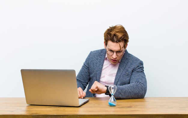 Joven empresario cabeza roja trabajando en su escritorio con un reloj. concepto de tiempo