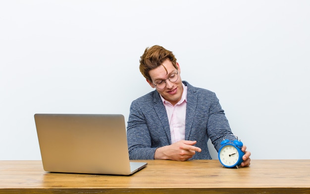 Joven empresario cabeza roja trabajando en su escritorio con un reloj. hora