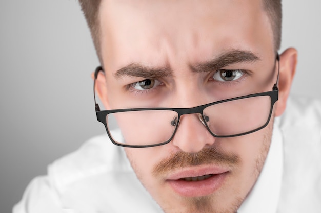 Joven empresario en camisa y gafas, conmocionado sobre fondo gris de estudio