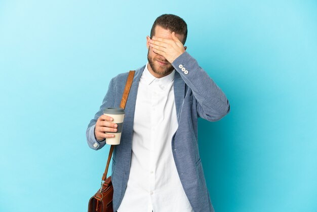 Joven empresario caucásico aislado en la pared azul que cubre los ojos con las manos. No quiero ver algo