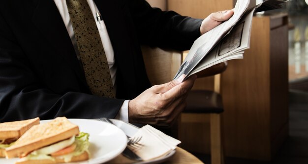 Joven empresario en una chaqueta negra leyendo un periódico en un café