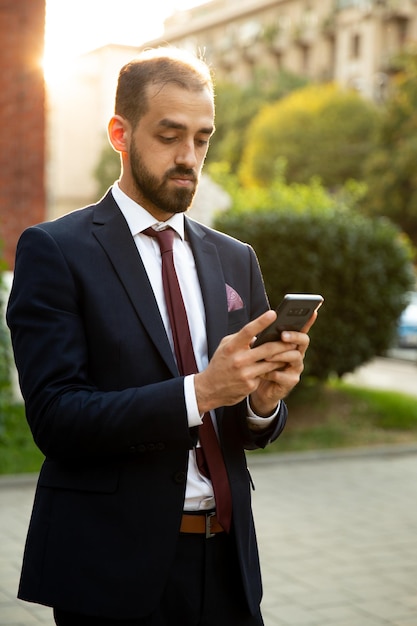 Joven empresario comprueba su correo electrónico en el teléfono. Atmósfera de la puesta del sol y de la ciudad