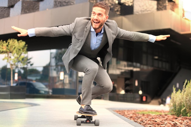 Joven empresario confiado en traje de negocios en longboard apresurándose a su oficina en la calle de la ciudad