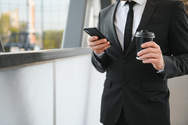 Joven empresario confiado usando teléfono celular y bebiendo café en la ciudad