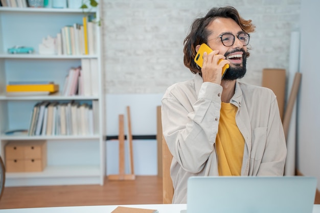 Joven empresario creativo hablando por teléfono riéndose sonriendo en su moderno espacio de trabajo en casa