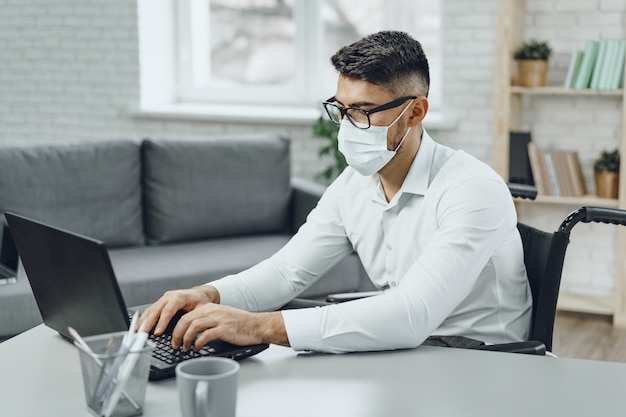 Joven empresario discapacitado haciendo su trabajo y usando mascarilla médica