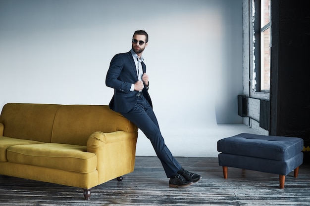 Joven empresario elegante líder en el interior de la oficina con gafas de sol mirando a un lado pensativo