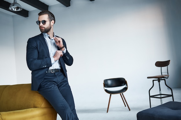 Joven empresario elegante líder en el interior de la oficina con gafas de sol mirando a un lado pensativo