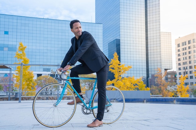 Joven empresario elegante que va a trabajar en bicicleta frente al distrito financiero