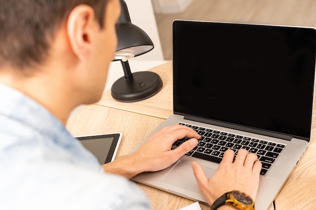 Joven empresario enfocado que realiza videollamadas con clientes en una laptop. Hombre milenario concentrado en anteojos dando clases educativas en línea, consultando al cliente.