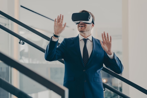 Joven empresario europiano emocionado en ropa formal de pie en el interior de la oficina con auriculares Vr