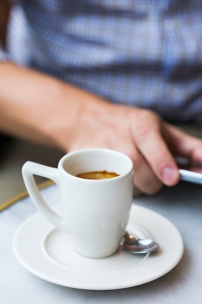 Joven empresario de éxito sentado en un café, tomando café por la mañana y usando el teléfono inteligente. Composición de estilo de vida con luz natural.