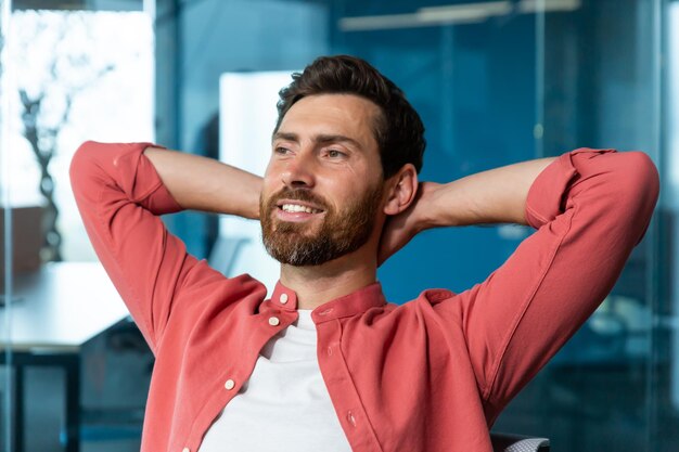 Foto el joven empresario exitoso descansa en la oficina, el hombre con camisa roja arroja las manos detrás de la cabeza y