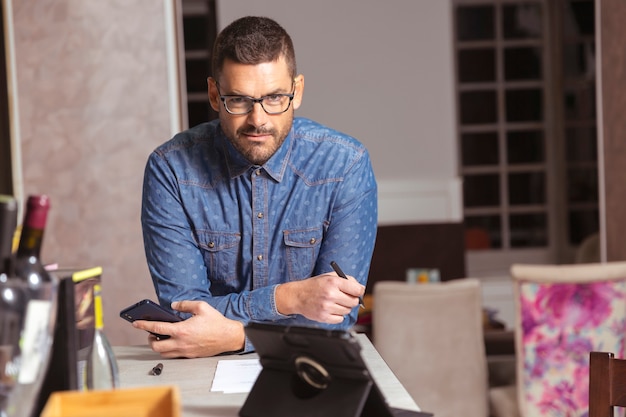 Foto joven empresario con gafas y camisa, apoyado en la barra de un bar de cócteles