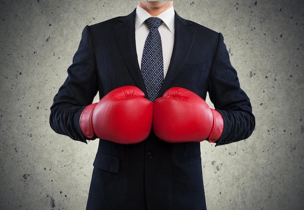 Joven empresario con guantes de boxeo rojos sobre fondo de pared gris