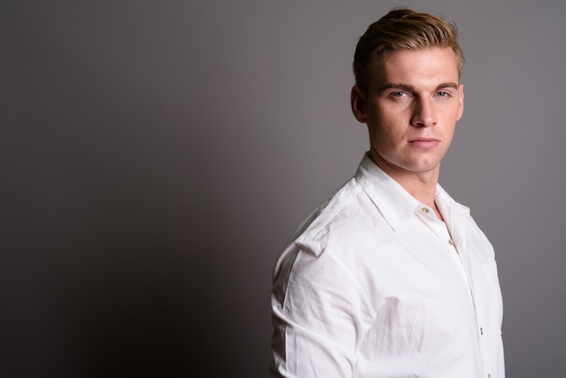 Joven empresario guapo con cabello rubio en la pared gris