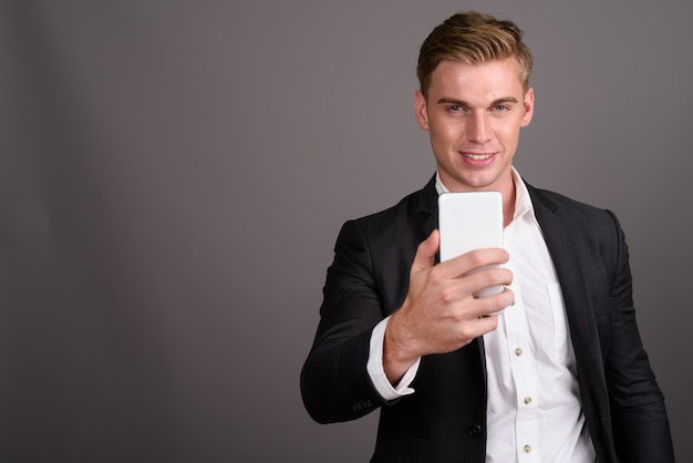 Joven empresario guapo con cabello rubio vistiendo traje en pared gris