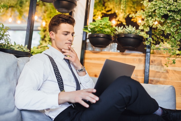 Joven empresario guapo con camisa blanca y corbata, portátil de trabajo en una oficina moderna y elegante.