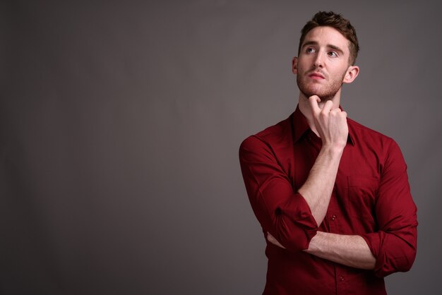 Joven empresario guapo con camisa roja contra gris