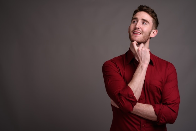 Joven empresario guapo con camisa roja contra gris