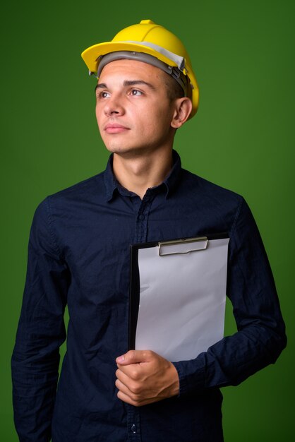 Joven empresario guapo con casco contra el fondo verde