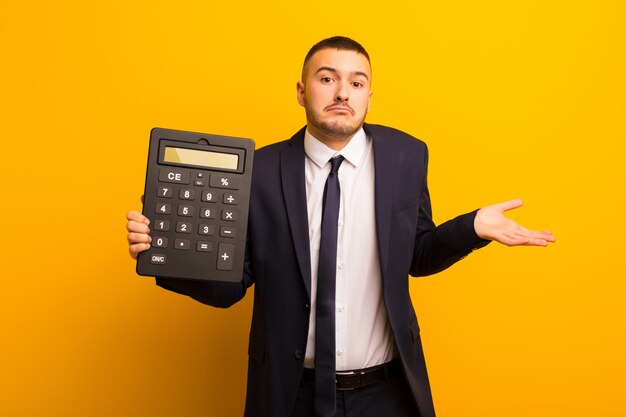 Joven empresario guapo contra el fondo plano con una calculadora