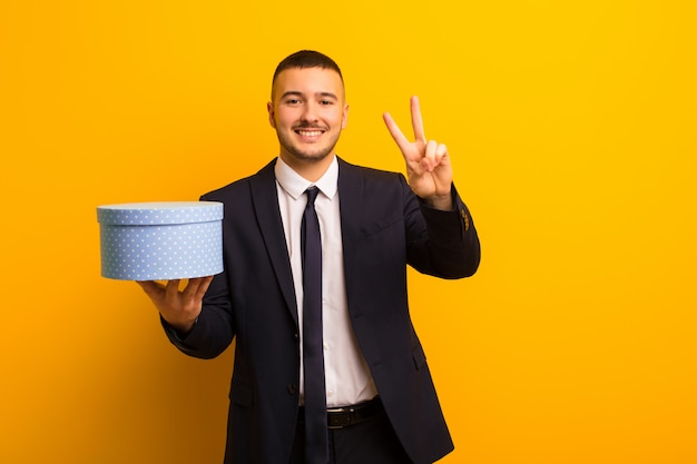 Joven empresario guapo contra la pared plana con una caja de regalo