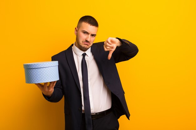 Joven empresario guapo contra la pared plana con una caja de regalo