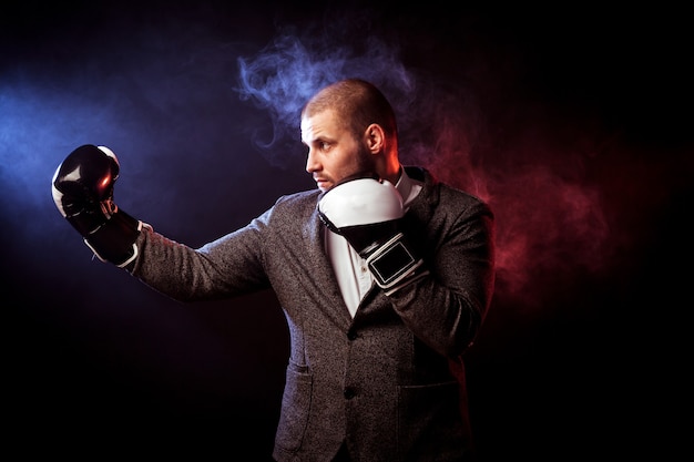 Joven empresario guapo en guantes blancos y negros de boxeo contra el humo rojo y azul