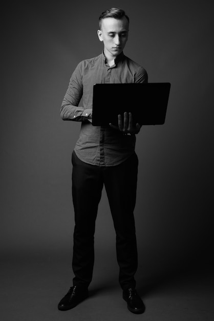 joven empresario guapo con ordenador portátil contra la pared gris. en blanco y negro