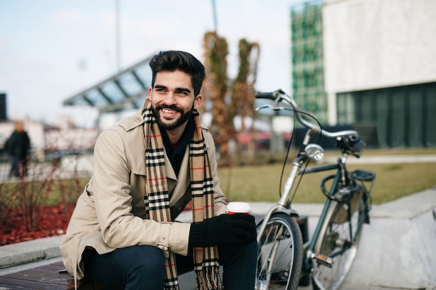 Joven empresario guapo sentado en un banco en la ciudad con una bicicleta. Protección del medio ambiente y concepto de transporte ecológico.