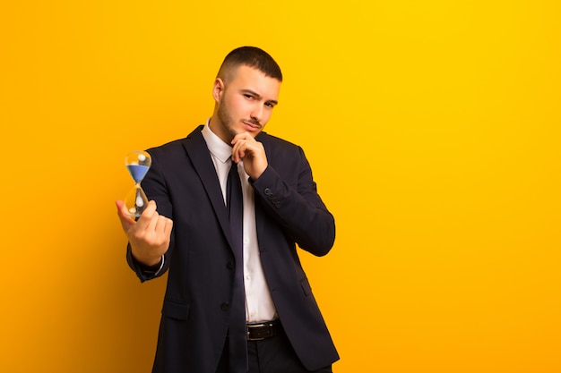 Joven empresario guapo sobre fondo plano con un reloj de arena temporizador