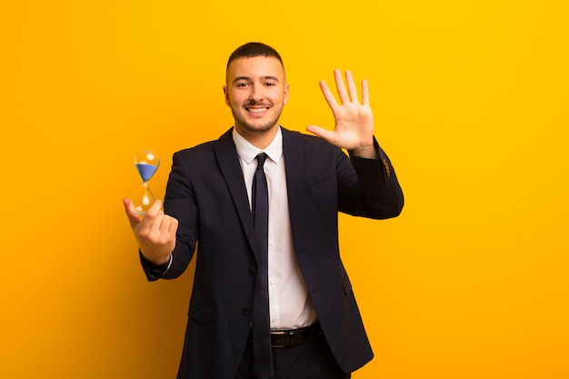 Joven empresario guapo sobre fondo plano con un reloj de arena temporizador