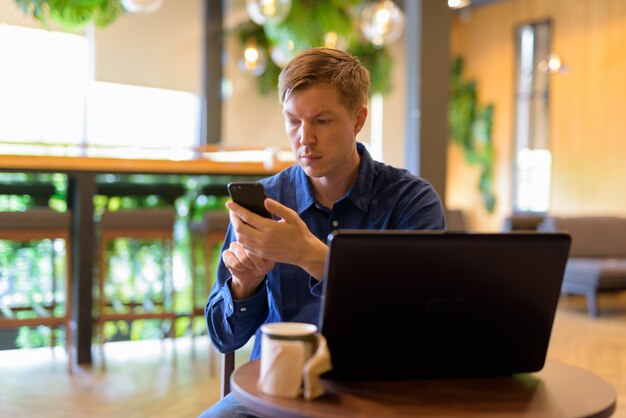 Joven empresario guapo con teléfono mientras trabajaba en la cafetería.