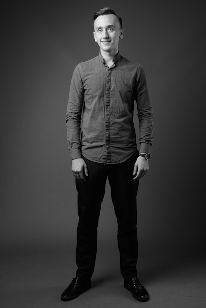 joven empresario guapo vistiendo camisa abotonada contra la pared gris. en blanco y negro