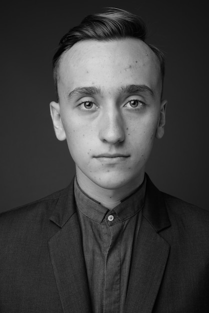 joven empresario guapo vistiendo traje contra la pared gris. en blanco y negro