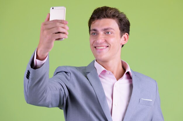 Joven empresario guapo vistiendo traje contra la pared verde