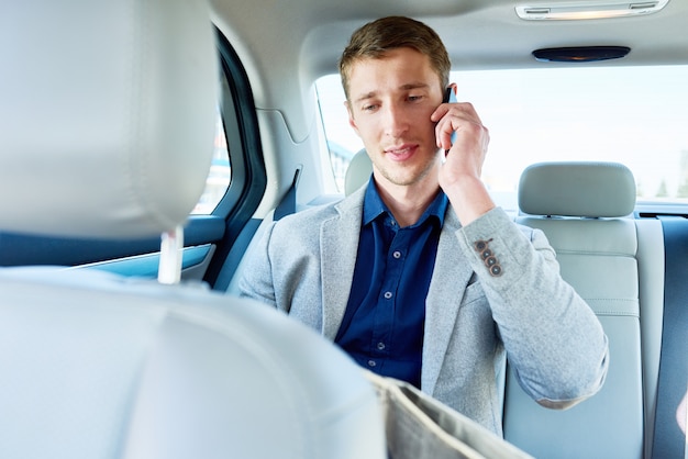 Joven empresario hablando por teléfono en el asiento trasero