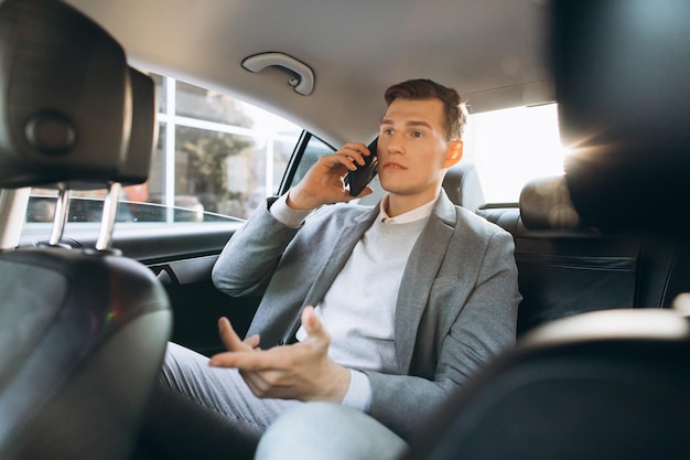 Joven empresario hablando por un teléfono móvil mientras está sentado en el asiento trasero de un coche