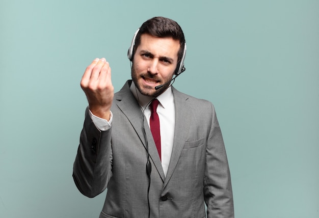 ¡Joven empresario haciendo capice o gesto de dinero, diciéndole que pague sus deudas! concepto de telemarketing