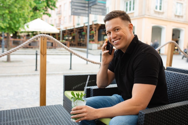 Joven empresario hombre sentado en la mesa del café de la calle con refrescante cóctel mojito