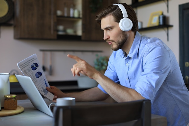 Joven empresario independiente concentrado que usa la computadora portátil para videoconferencia, trabajando de forma remota en línea en casa.