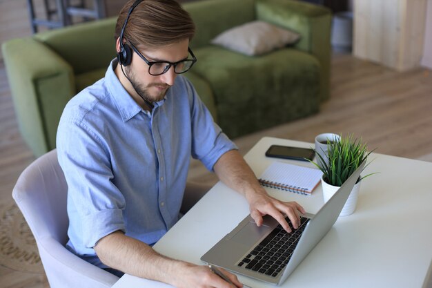 Foto joven empresario independiente concentrado que usa la computadora portátil para videoconferencia, trabajando de forma remota en línea en casa.