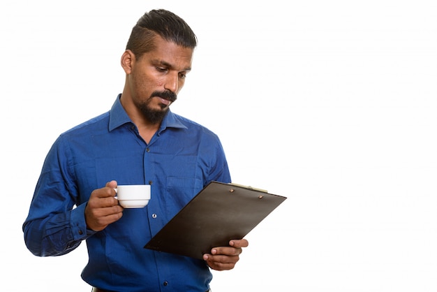 Joven empresario indio leyendo portapapeles mientras sostiene la taza de café