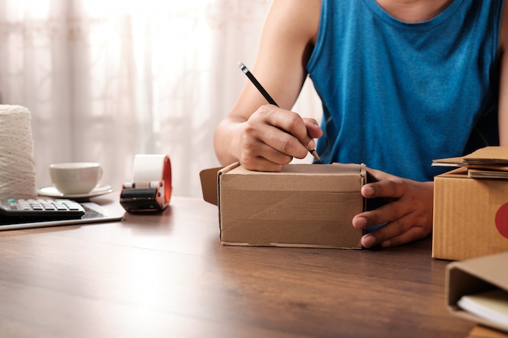 Foto joven empresario de inicio escribiendo la dirección en una caja de cartón en casa