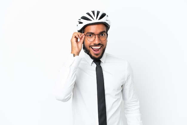 Joven empresario latino sosteniendo un casco de bicicleta aislado sobre fondo blanco con gafas y sorprendido